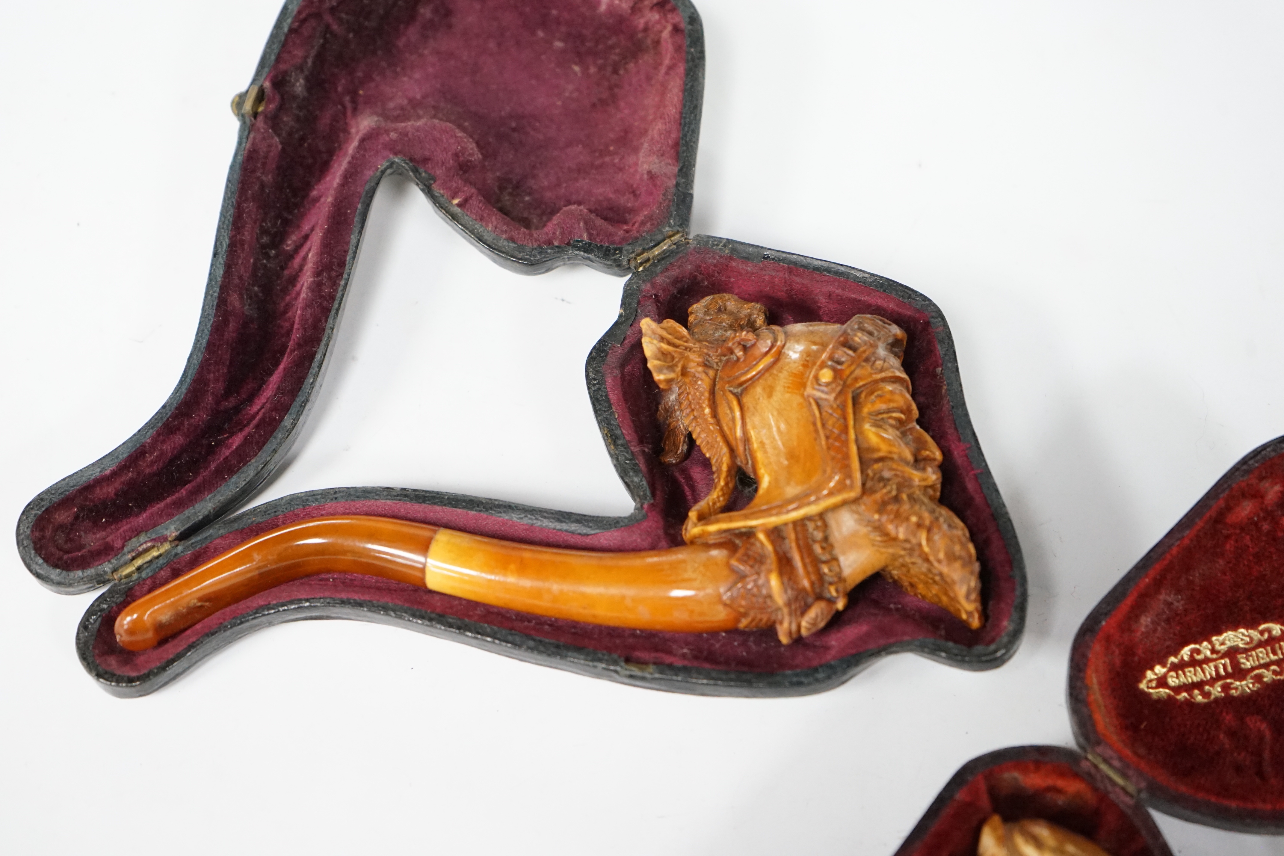 Two cased novelty Meerschaum pipes, their bowls modelled as an Arthurian knight and another a bearded man, both with amber mouthpieces, largest 16cm long